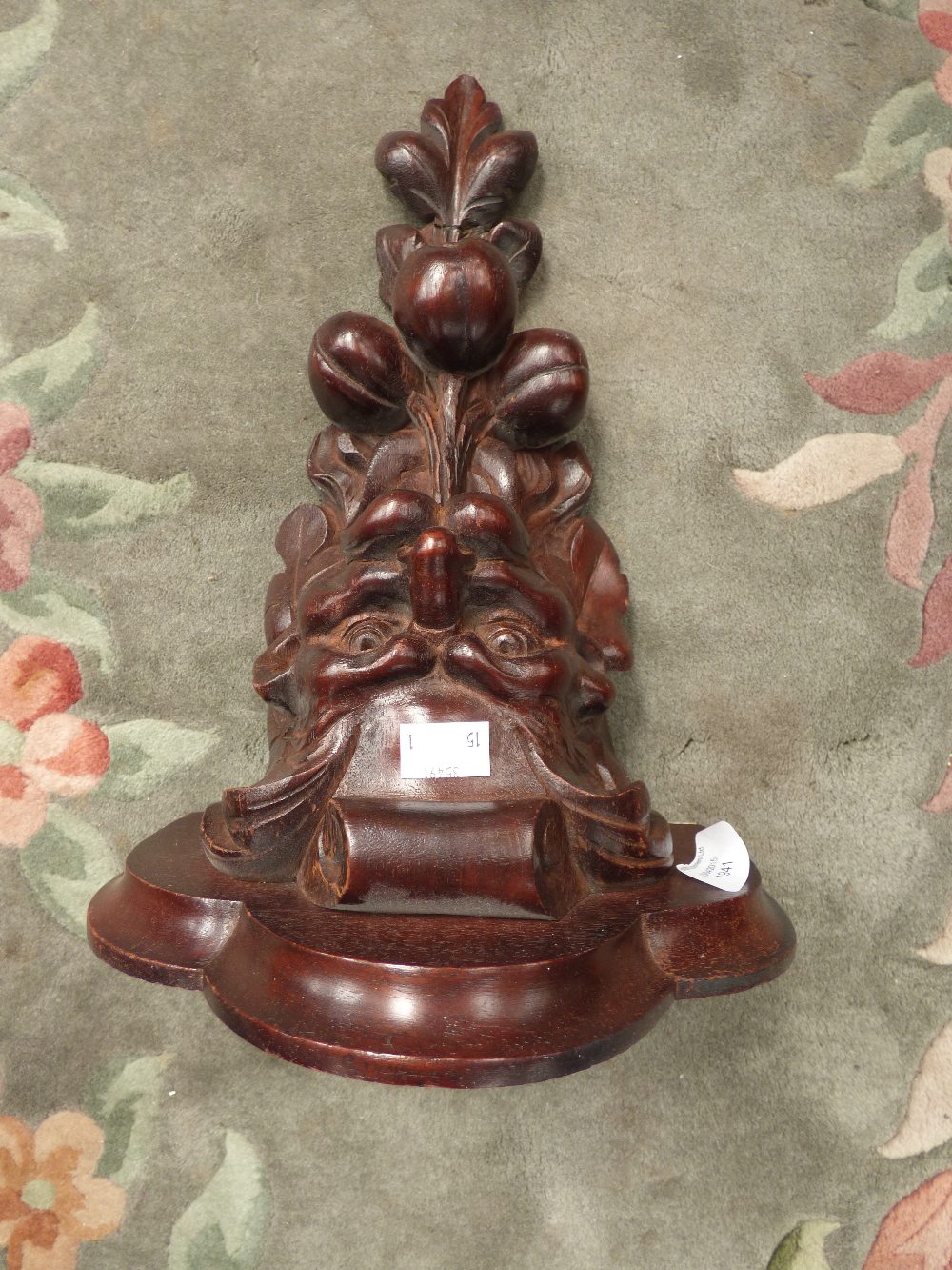 A carved mahogany bracket in the form of a grotesque mask with fruit hanging from the mouth