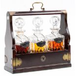 A three decanter tantalus, containing cut glass spirit decanters, dark stained veneer with brass