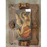 A carved and painted elm panel, with a heraldic wyvern and coat of arms within a shell scroll