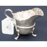 A George V silver cream jug raised on three scroll feet,