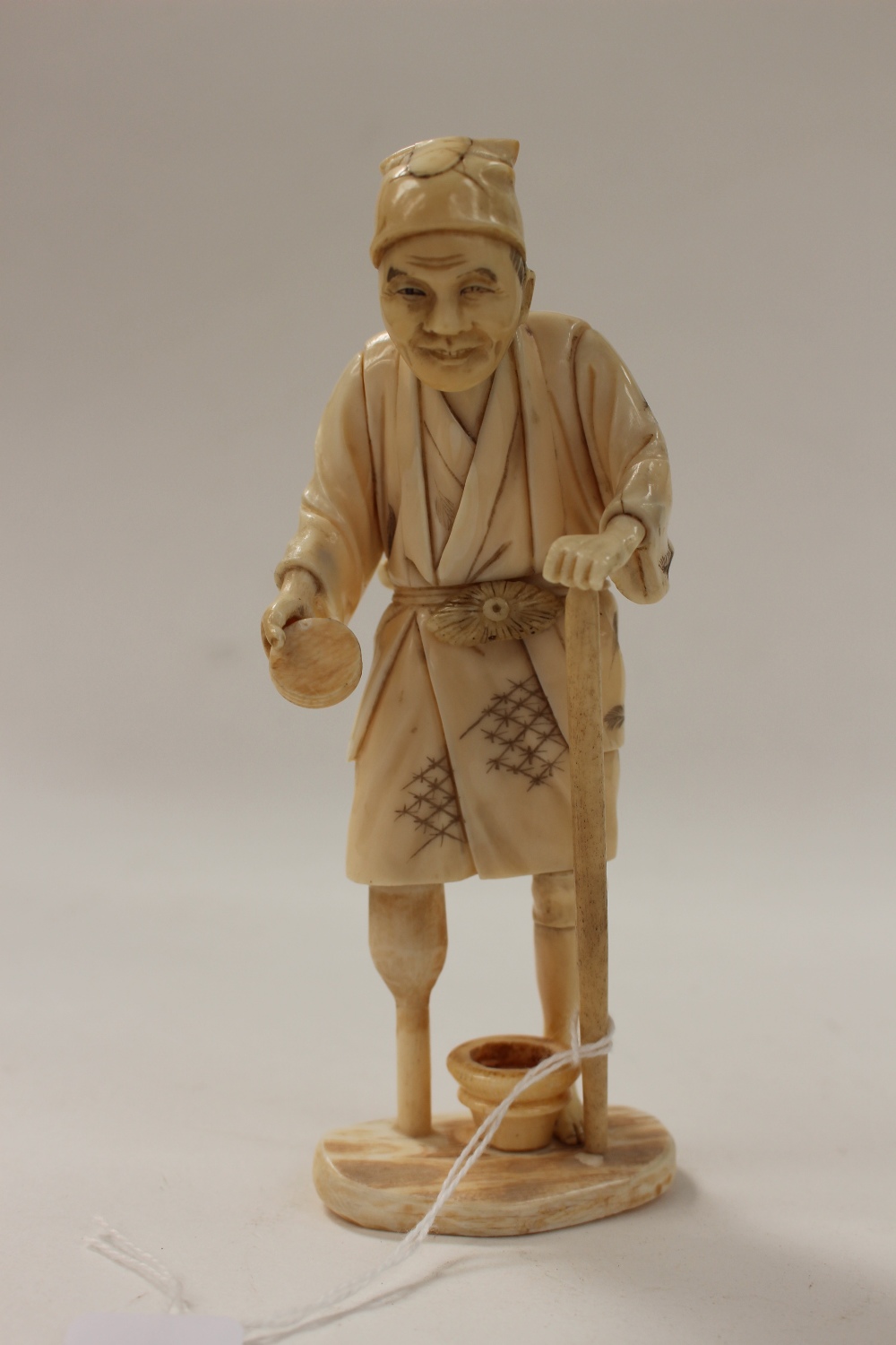 A Japanese carved ivory okimono of a man with a wooden leg,