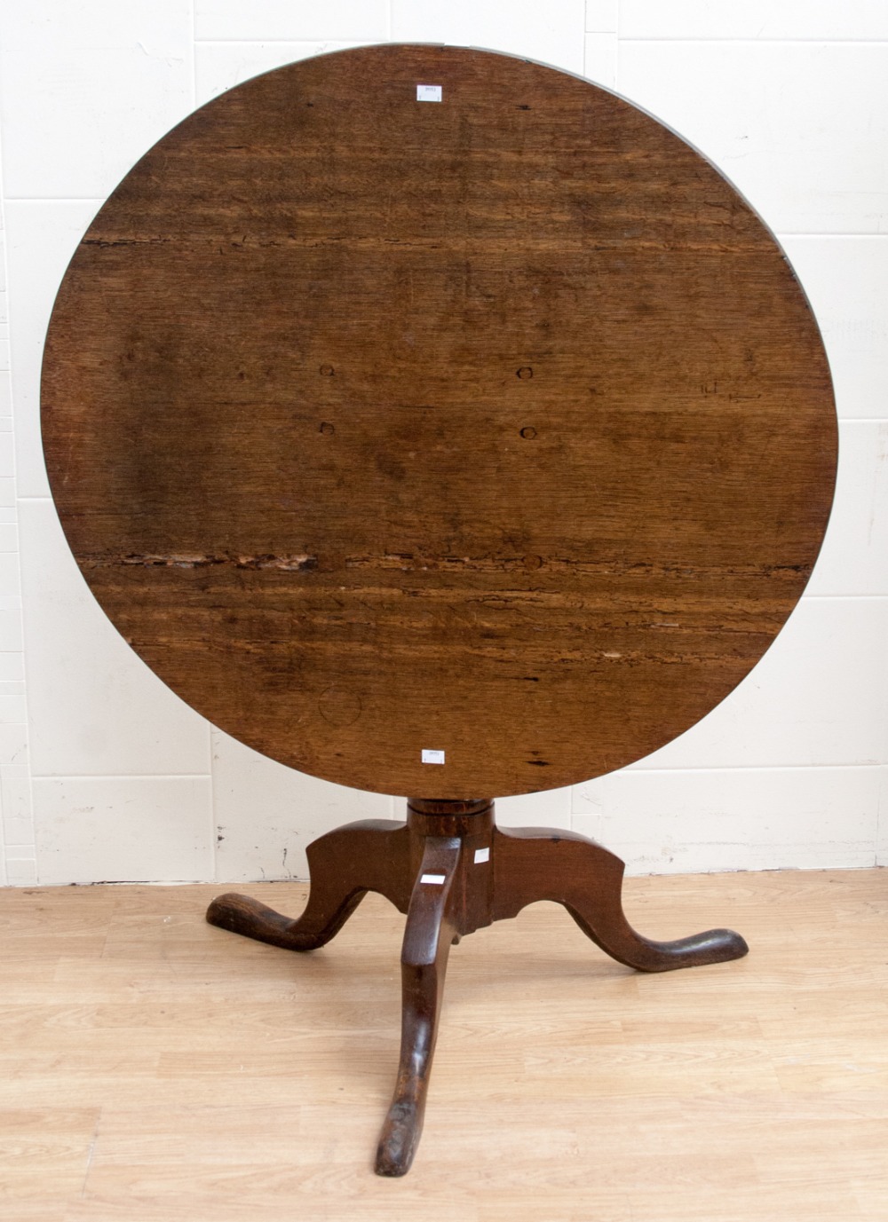 A George III oak tilt top tripod table, the circular top raised on a turned column,