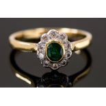 An emerald and diamond cluster ring with oval emerald in rub over setting within border of ten