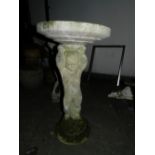 A stone birdbath, raised on a circular b