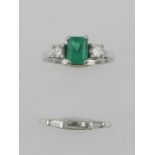 A white metal, emerald and diamond engagement ring, set central emerald cut stone flanked by two