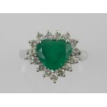 A white metal, emerald, and diamond set heart-shaped dress ring, centred with a heart-shaped emerald