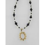 A yellow metal and pearl mounted oval pendant, suspended on a black bead and white pearl necklace,