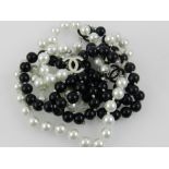 A Chanel style black and white pearl necklace, having enamelled fifi embellishment.