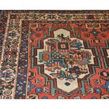 A Bakhtiari brick red ground carpet woven six lobed floral medallions within a triple border, 325cm