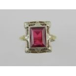 A yellow and white metal Art Deco style dress ring, set with an emerald cut ruby, within an