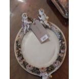 An early 20th century Dresden porcelain oval toilet mirror, the frame surmounted with amorini and