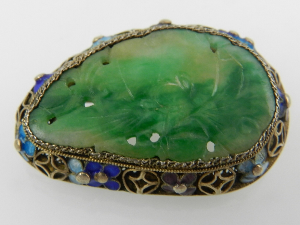 A silver, jade, and enamel brooch, the pierced green jade plaque set in an openwork mount decorated