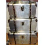 A graduated set of three aviator-style trunks, wood-bound aluminium exteriors with hinged lids,