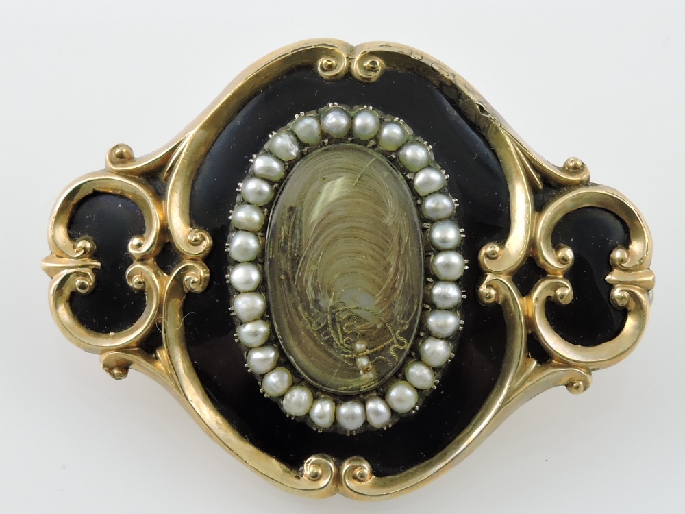 A Victorian yellow metal, enamel and seed pearl memorial brooch, centred by an oval mount of hair,