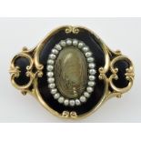 A Victorian yellow metal, enamel and seed pearl memorial brooch, centred by an oval mount of hair,