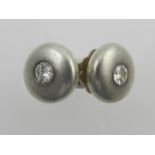 A pair of white metal round ear studs, each set with a central diamond.