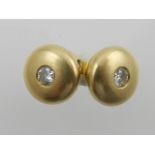 A pair of yellow metal rounded ear studs, each set with a central diamond.