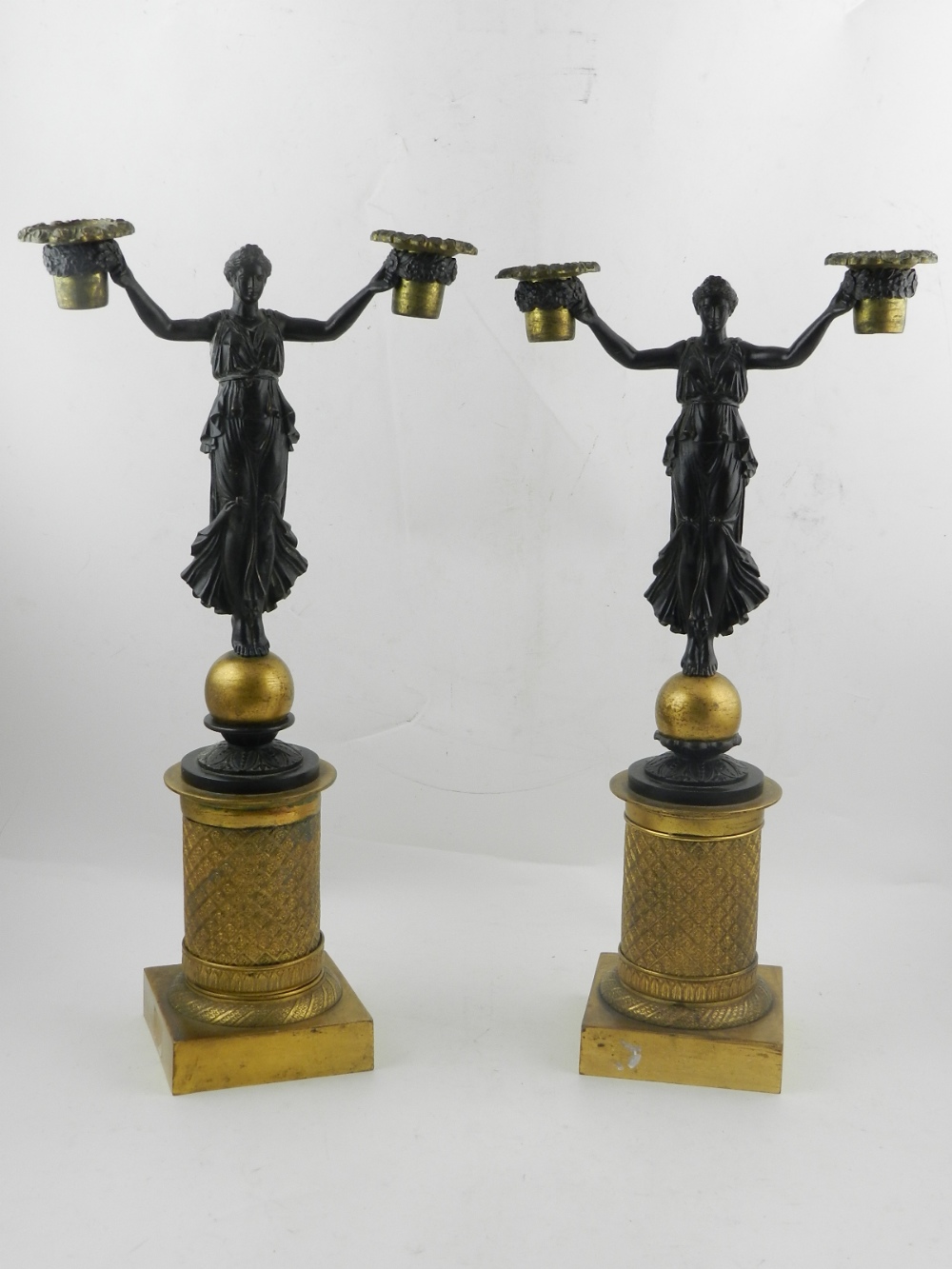 A pair of bronze candlesticks, in the form of a woman holding her arms,