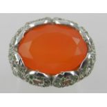 A white metal cocktail ring, set with a large carnelian, the mount set with small green stones.