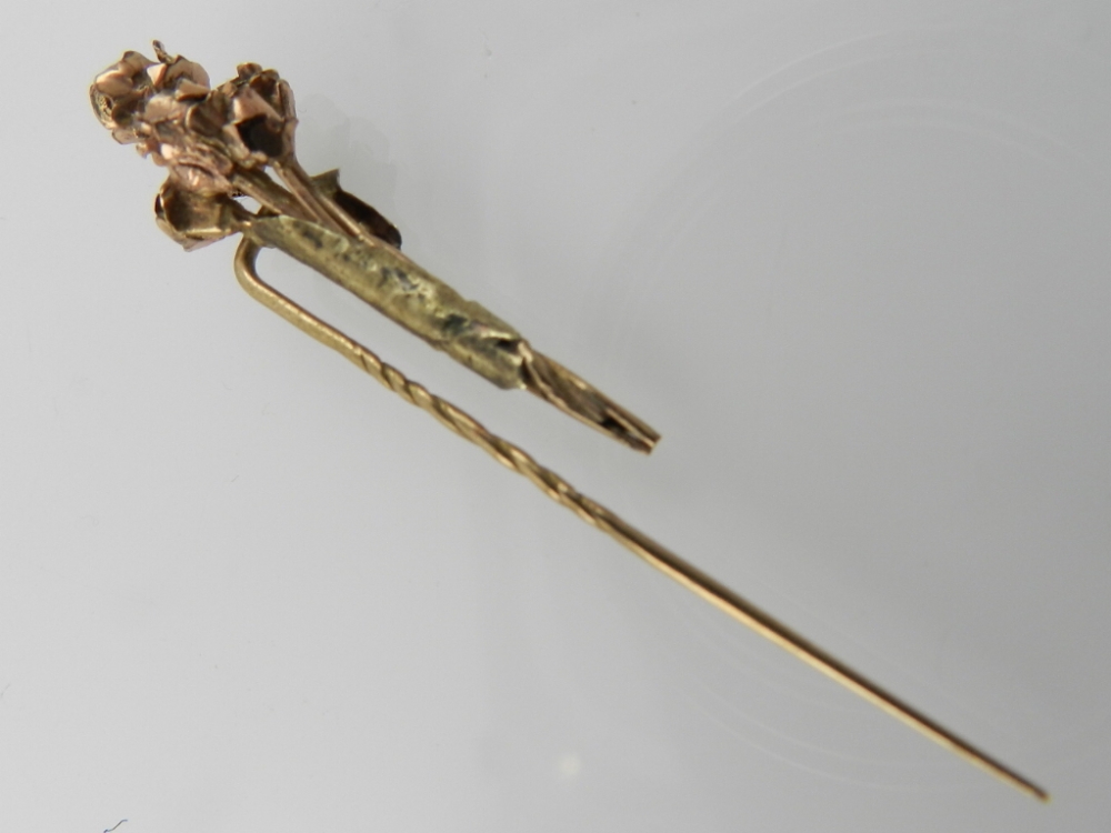 A yellow metal tie pin designed as a boutonniere of roses.