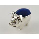 A white metal pin cushion in the form of a preoccupied pig, with blue velvet cushion, 19g.