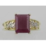 A yellow metal and ruby ring, the emerald cut ruby flanked by openwork shoulders with diamond