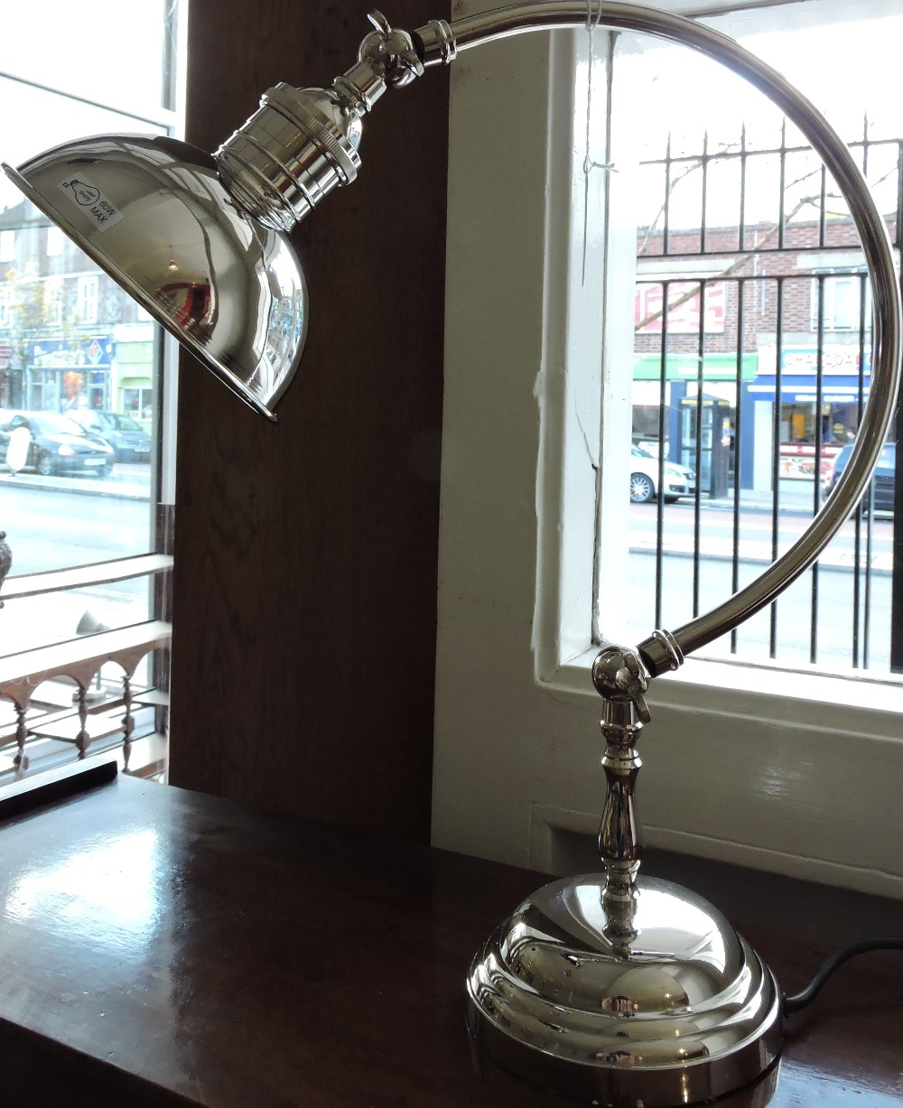 A plated desk lamp with circular shade on curved arm and stepped base.