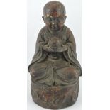 A bronze figure of a monk, seated cross-legged holding a small barrel,