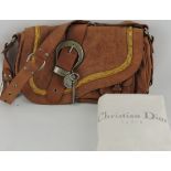 A tan leather Dior saddle bag, with white cloth storage bag.