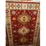 A Kazak red ground rug, having three medallions to centre on a geometric patterned ground, multi-