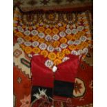 A ceremonial robe, decorated with yellow, white and black scrolls on a red ground, fringed.