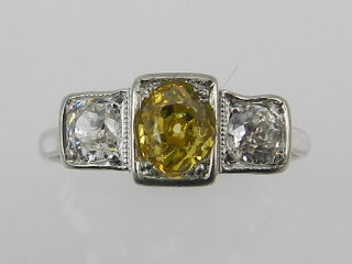 A white metal and three stone diamond ring, set central yellow diamond of approx. 0.