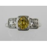 A white metal and three stone diamond ring, set central yellow diamond of approx. 0.