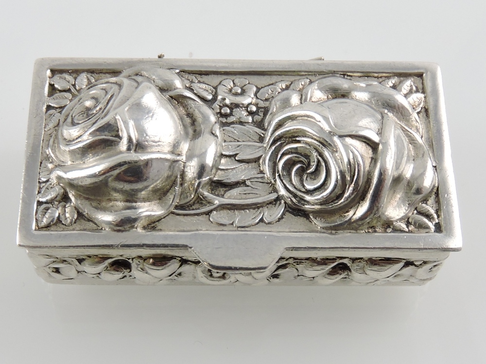 A silver pill box decorated with roses and trailing vines.