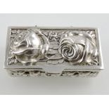 A silver pill box decorated with roses and trailing vines.