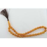 An amber necklace of uniform oval beads and turned drop with brown tassel, L. 46cm.
