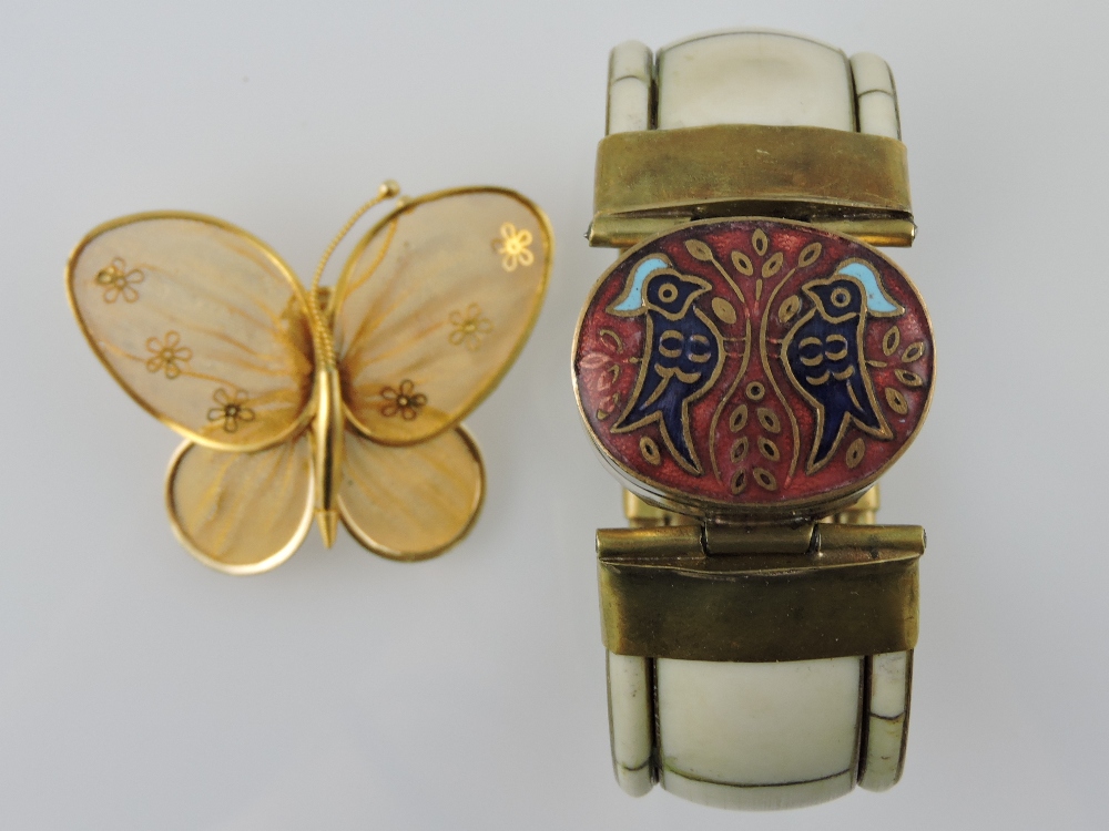 A bone bangle incorporating an enamelled oval box, together with a gilt filigree butterfly, (2).