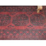 An Afghan red ground hall rug woven central octagonal medallions within a wide border,