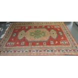 A kazak brick red ground rug woven with birds and geometric devices within a wide multiborder,