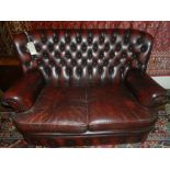 A Chesterfield style two seater sofa, upholstered in red burgundy, raised on casters.