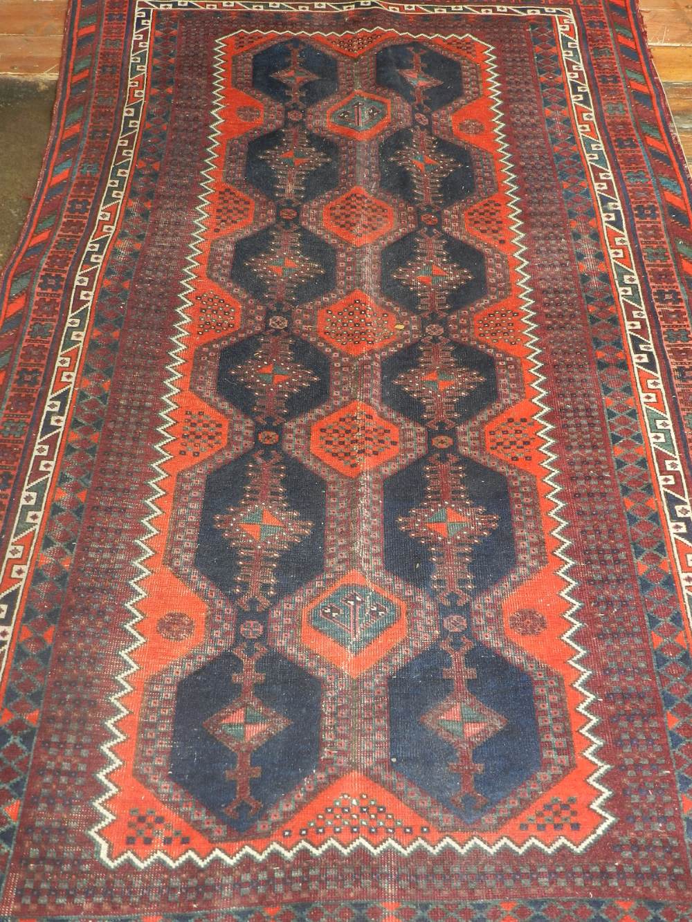A Caucasian red ground rug, having two rows of six medallions to centre within many borders. L.