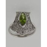 An 18 carat white gold, diamond, and peridot ring, of semi shield form,