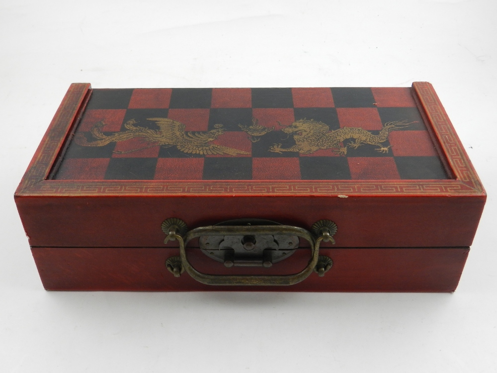 A Chinese red lacquered chess set, decorated with gilt dragons, having painted wooden pieces. H.