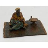 A cold painted bronze of an Arabian man sitting on a rug, in the style of Bergman.