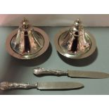 A pair of Arabic white metal butter dishes with bell shaped lids, together with two knives, (4).