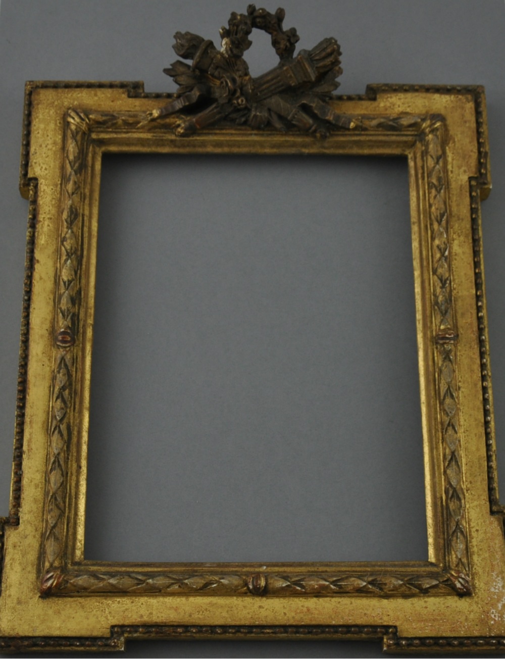 A small gilt picture frame, rectangular with projecting square corners and a trophy surmount,