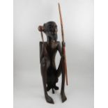 An African carved hardwood tribal figure of a seated male holding a spear.