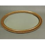 An oval wall mirror with beveled plate and faux walnut frame, 87cm.