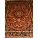 A red ground Kashan style rug, having central medallion on a floral ground, multi-bordered and