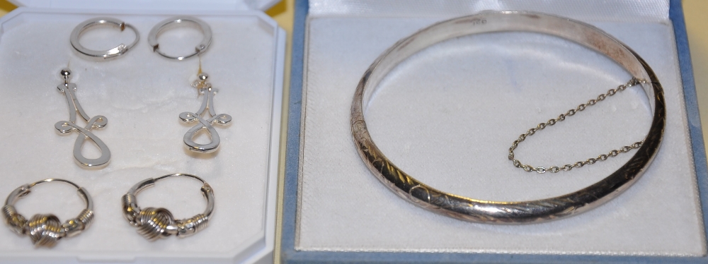An engraved silver bangle together with three pairs of assorted silver hoop and pendant earrings